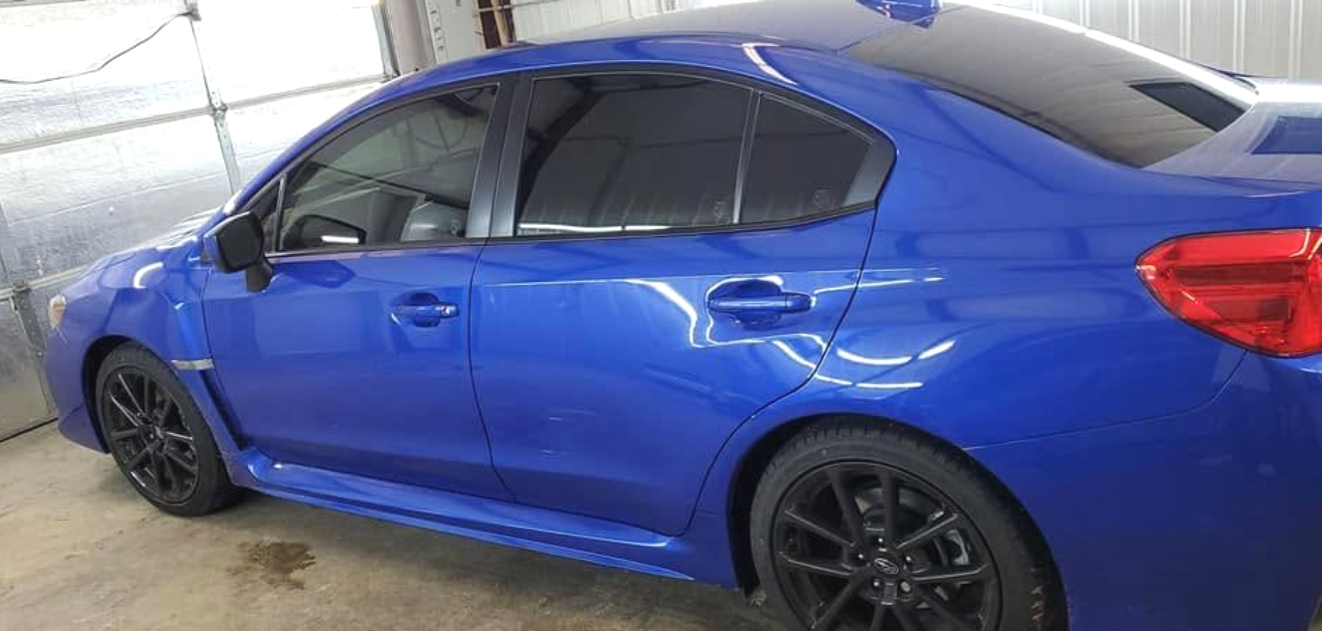 Blue sedan parked indoors, side view with black wheels and tinted windows