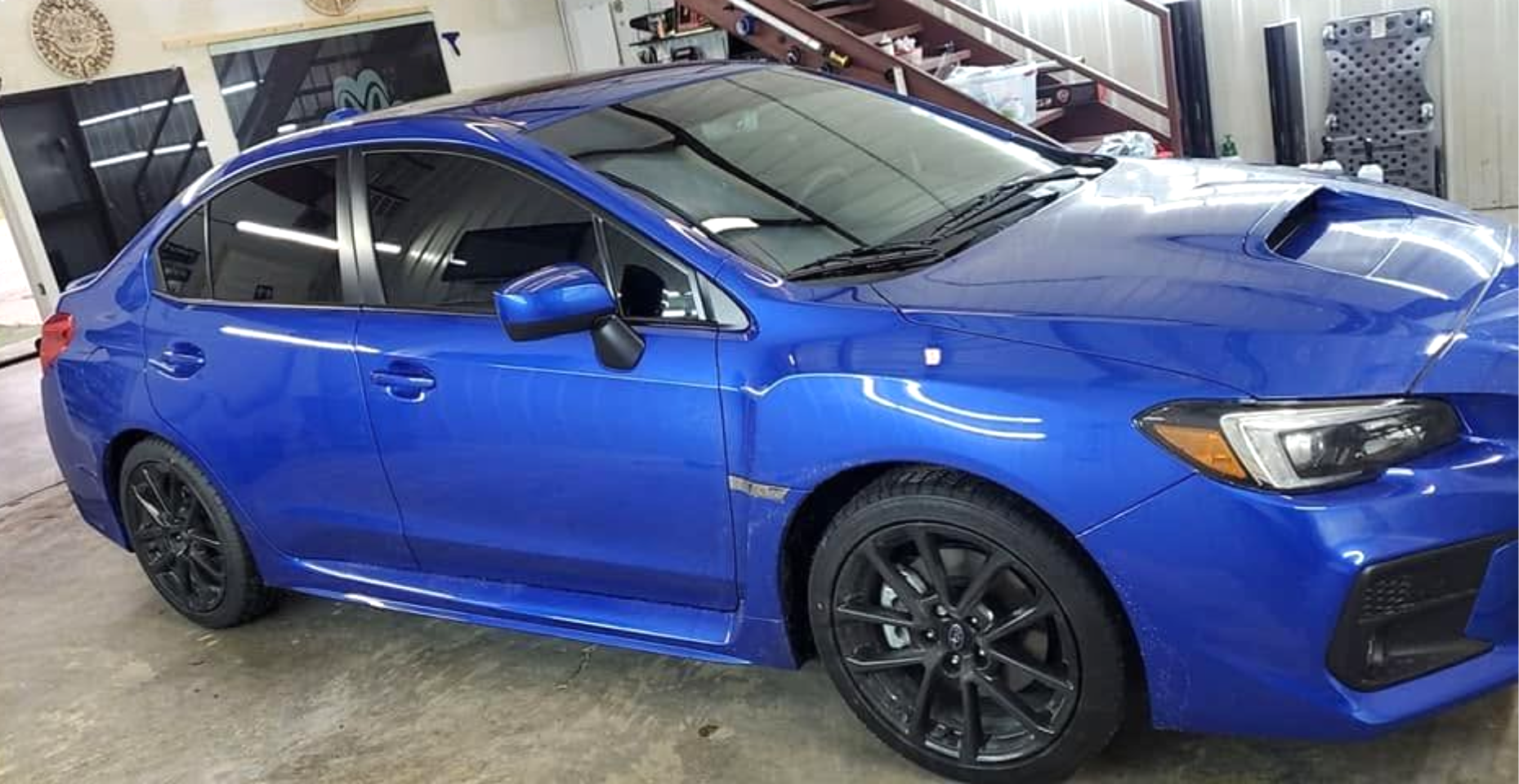 Blue sports sedan parked indoors in a garage, shown from the front side.