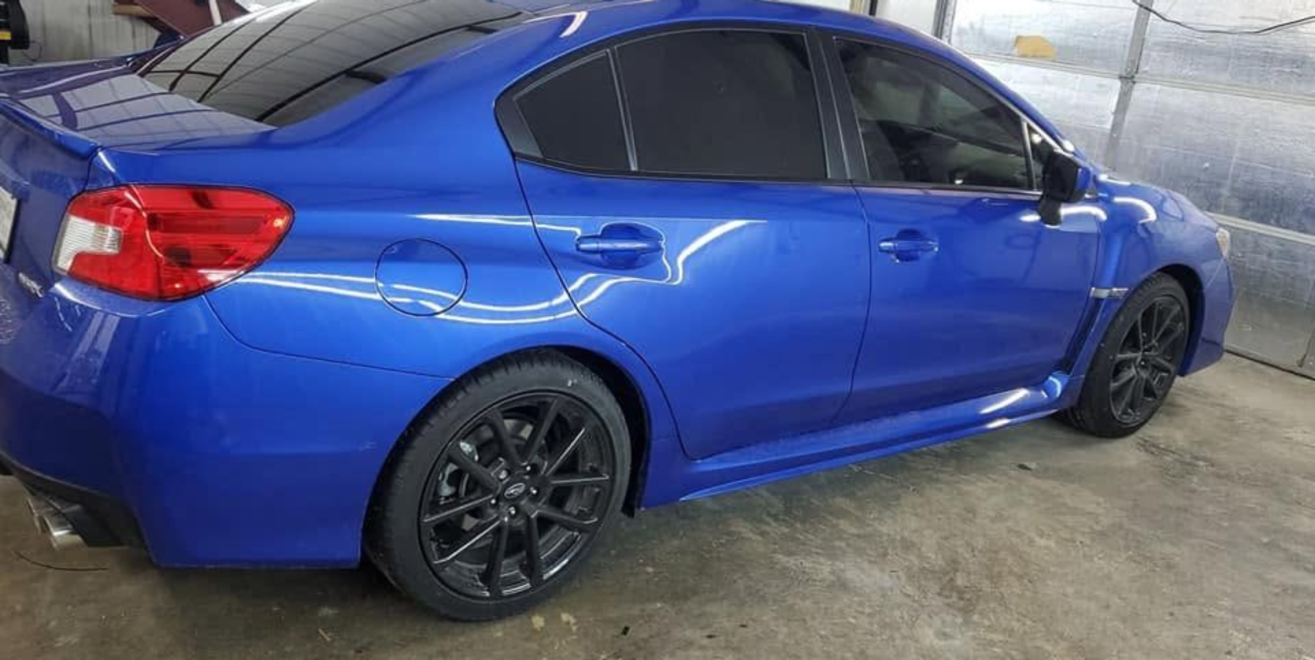 Blue sedan with black rims parked on a wet concrete surface indoors