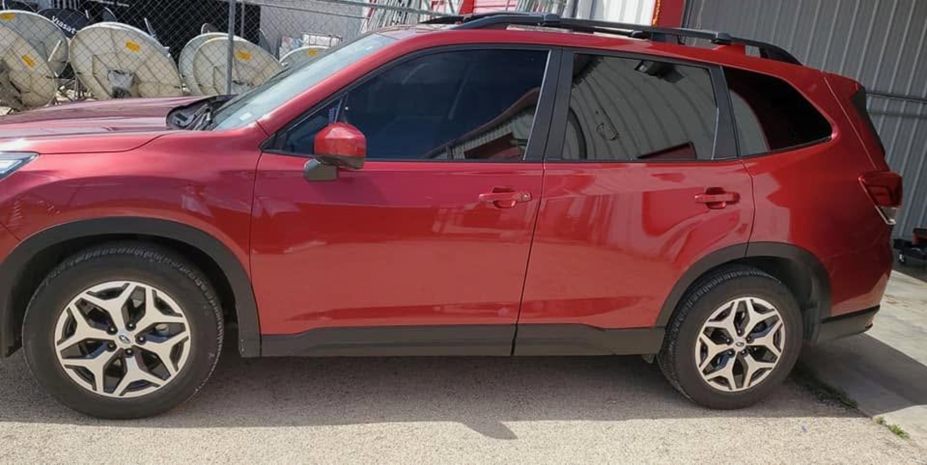 Red SUV parked outdoors in front of industrial equipment, side view.