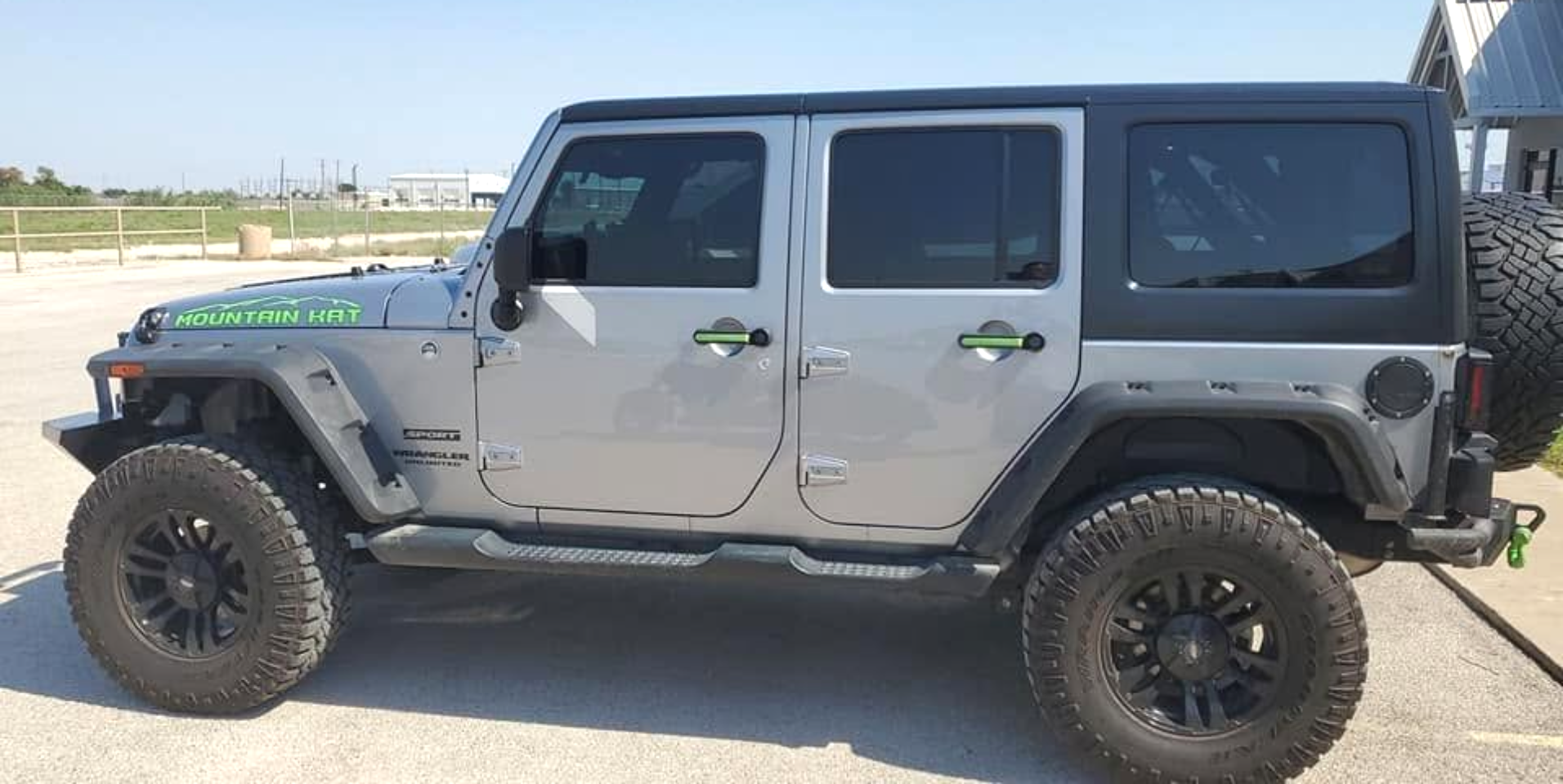 Gray Jeep Wrangler parked outdoors on a sunny day, side view with lifted suspension and large black tires