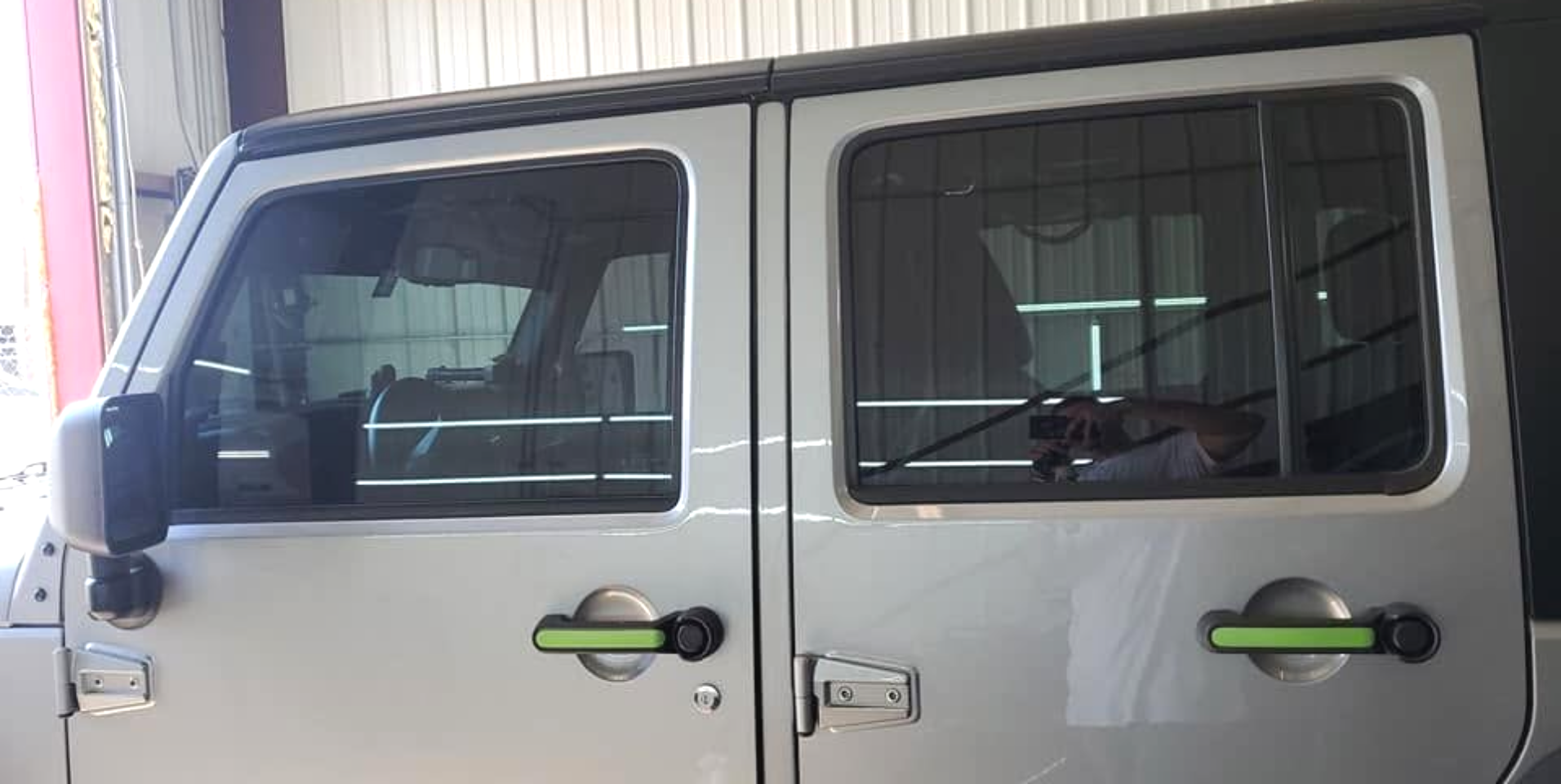 Silver SUV with dark-tinted windows and green door handles parked beside a corrugated wall
