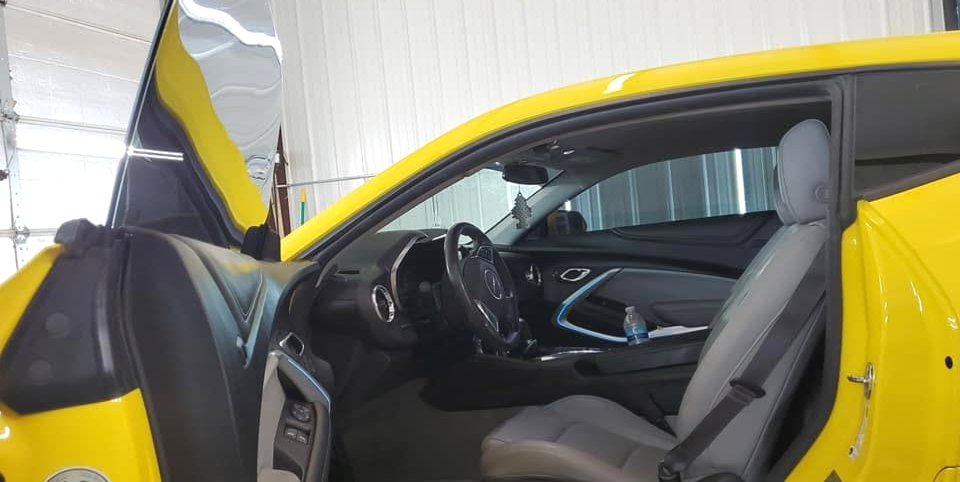 Open car door revealing a gray interior and dashboard, with a yellow exterior in a garage.
