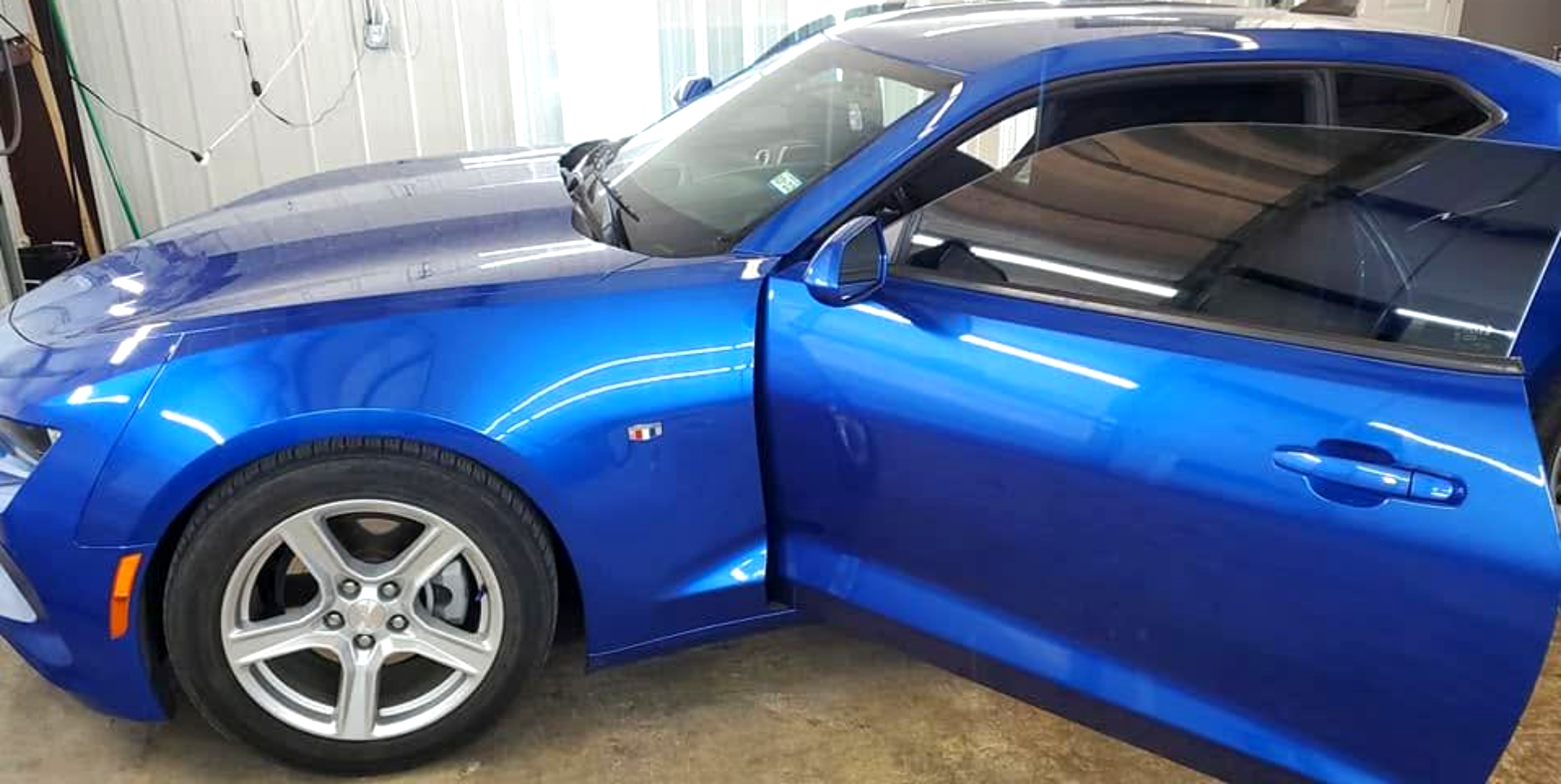 Blue sports car with open passenger door parked in a garage