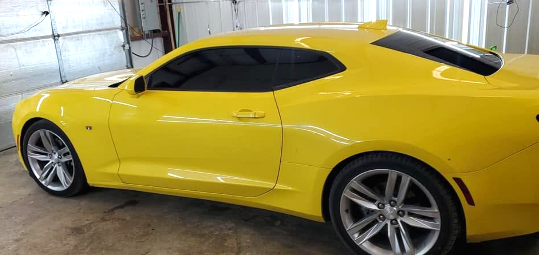 Yellow sports coupe in a showroom, side view with black tinted windows and silver alloy wheels