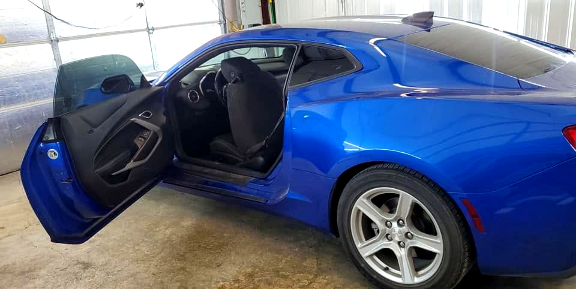 Blue sports car with driver door open, shown in a garage.