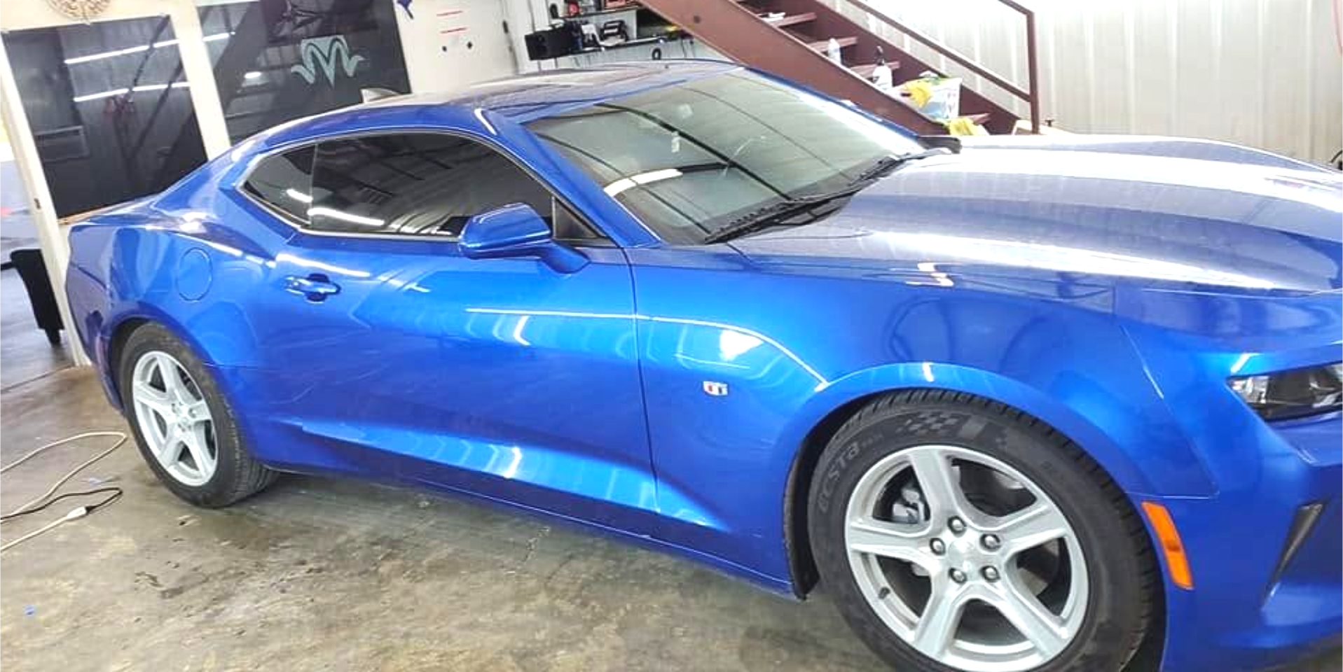 Blue sports coupe parked indoors, side view with silver rims and a black roof.