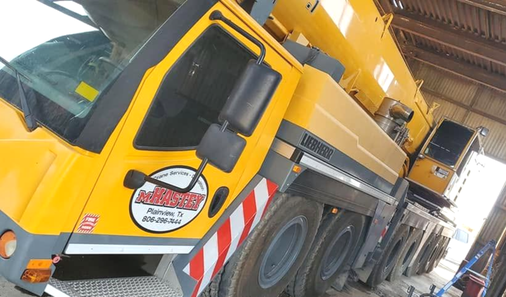 Yellow crane truck with extended boom parked indoors at a construction site.