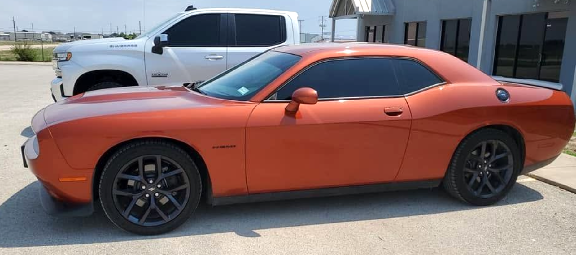 Orange sports coupe parked beside a white pickup truck outside a building.