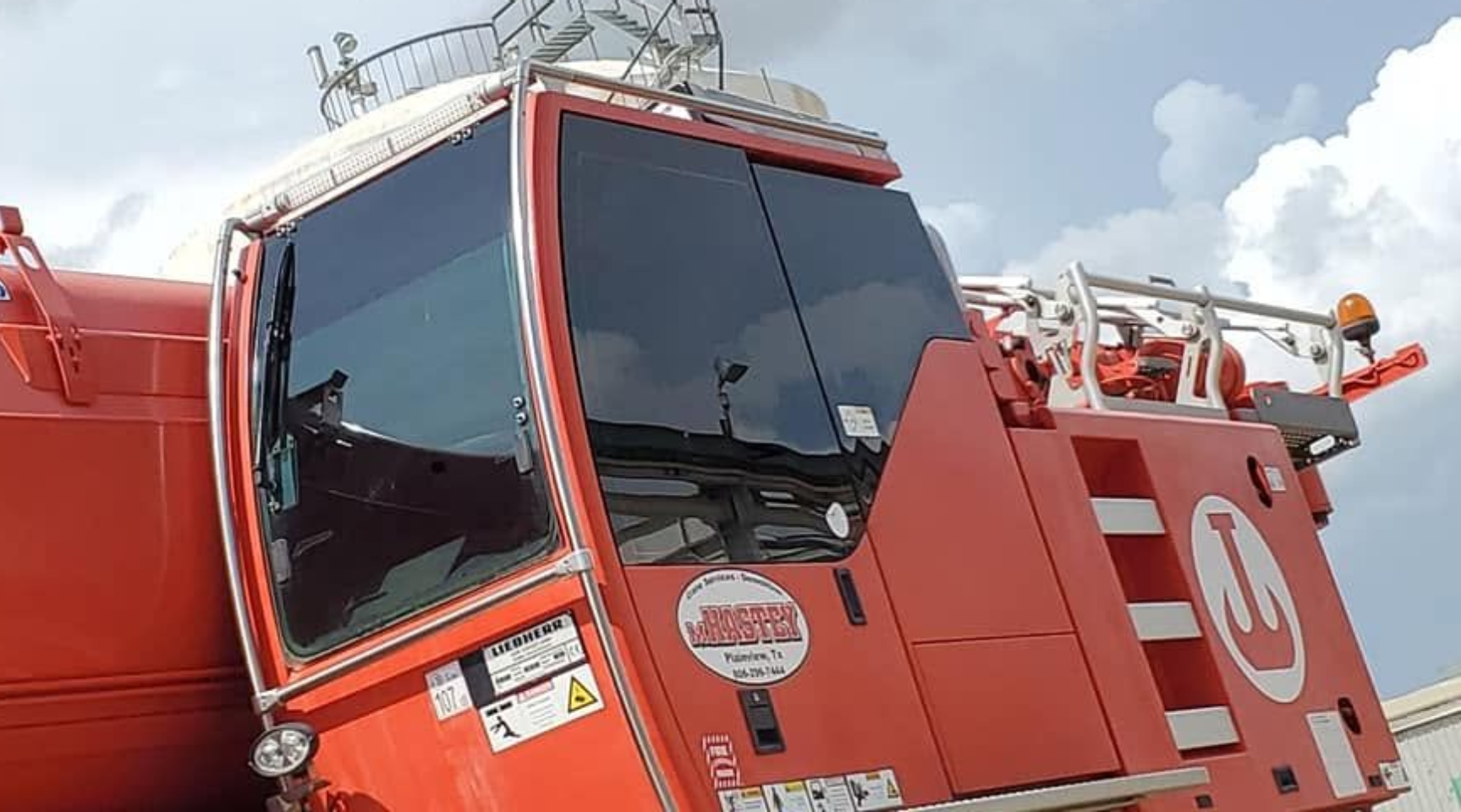 Red industrial truck cab with tinted windshield and white stripes against a cloudy sky