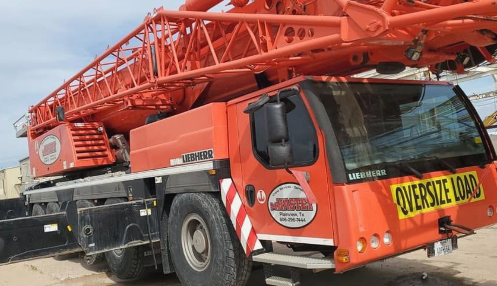 Red mobile crane truck with yellow “OVERSIZE LOAD” sign on the front, parked outdoors