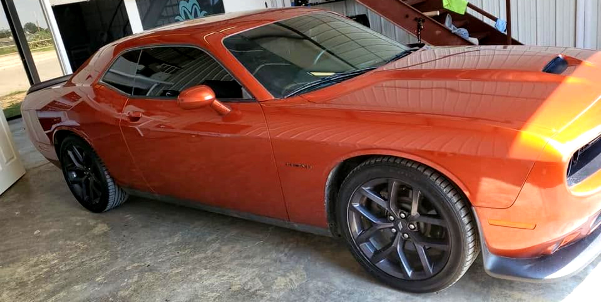 Orange sports coupe parked indoors, side view with black rims and white racing stripes on the hood
