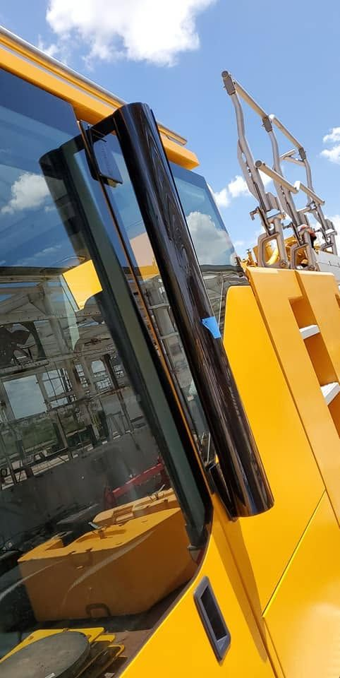 Yellow construction vehicle with raised front cab and hydraulic arms against a blue sky