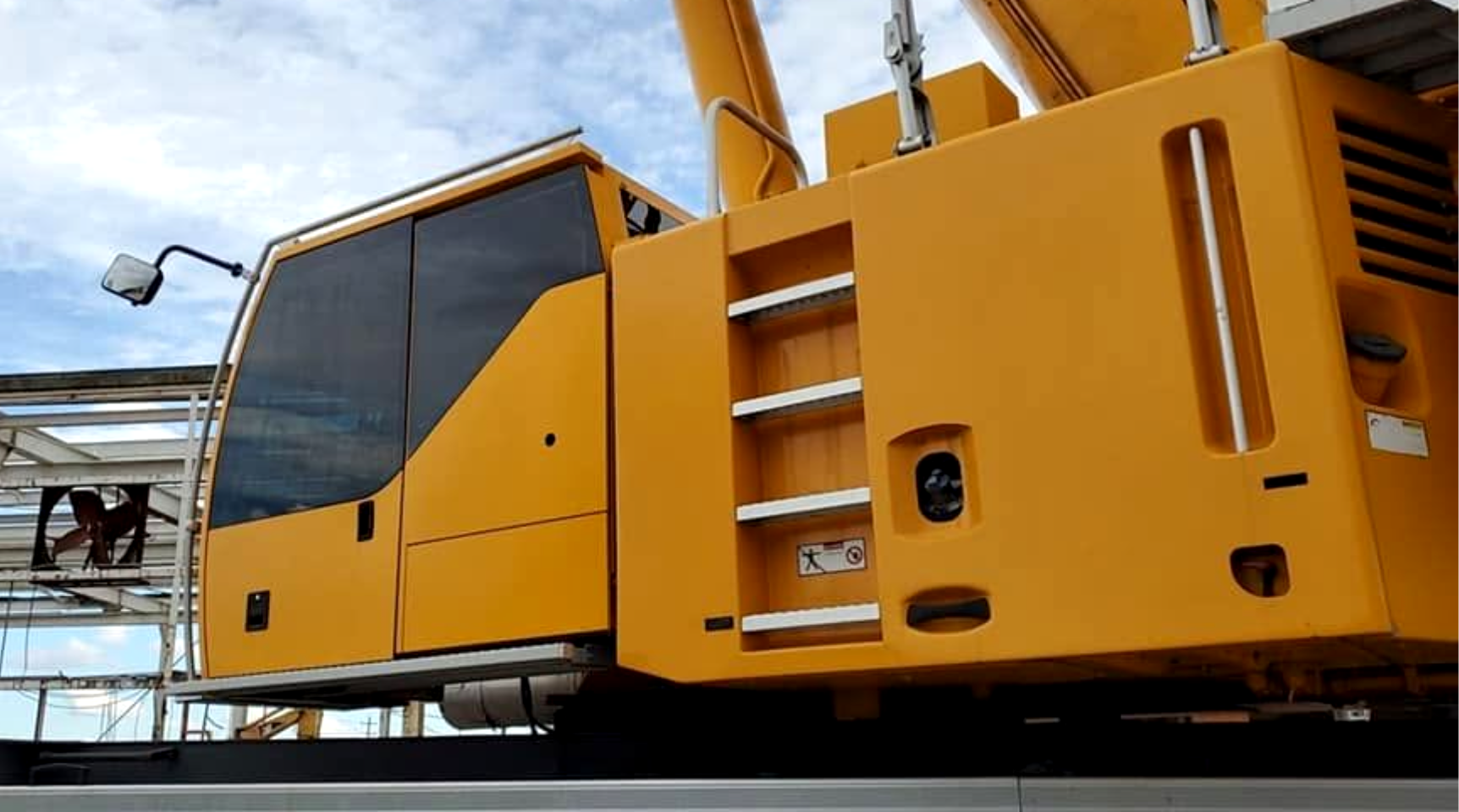 Yellow industrial crane on a flatbed truck, viewed from the side at a construction site