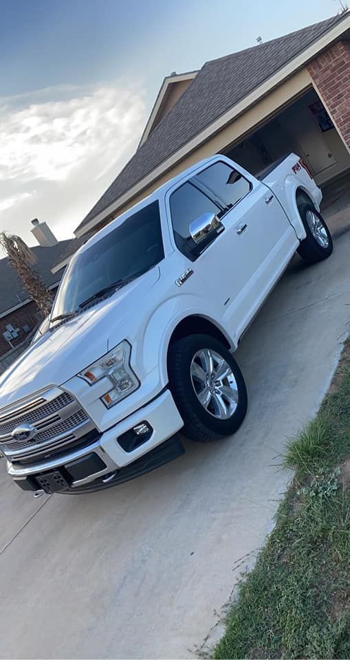 White Ford pickup truck parked in a driveway beside a brick house under a cloudy sky