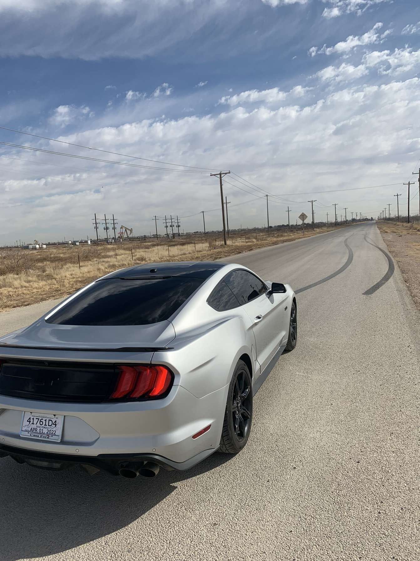 Silver sports car parked on a gravel roadside under a cloudy sky, with power lines in the distance