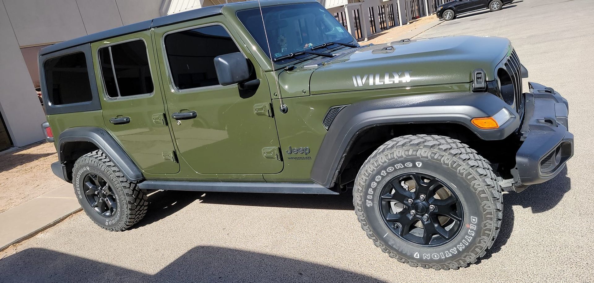 Green Jeep Wrangler parked outdoors on pavement, side view with black wheels and off-road tires.