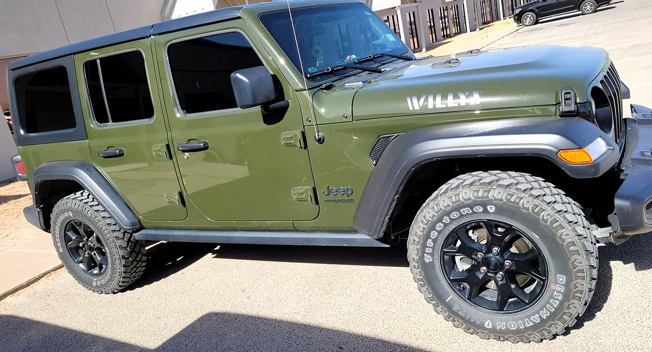 Green Jeep Wrangler parked on pavement, side view with black off-road tires and hardtop roof