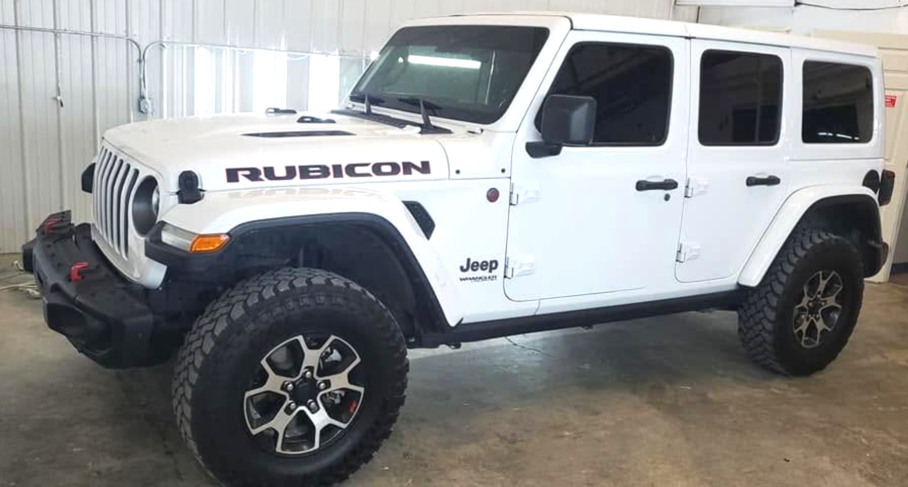 White Jeep Rubicon SUV parked indoors, side view with black off-road tires