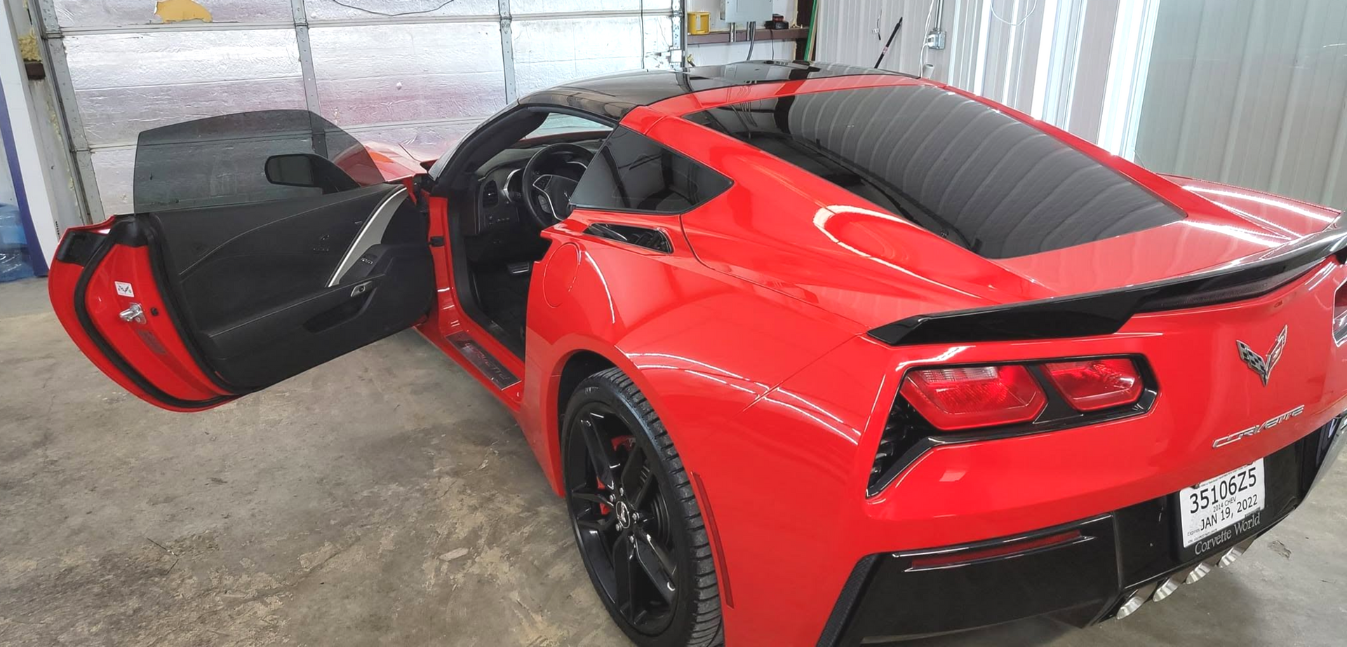 Red sports car with driver door open in a garage, rear and side view