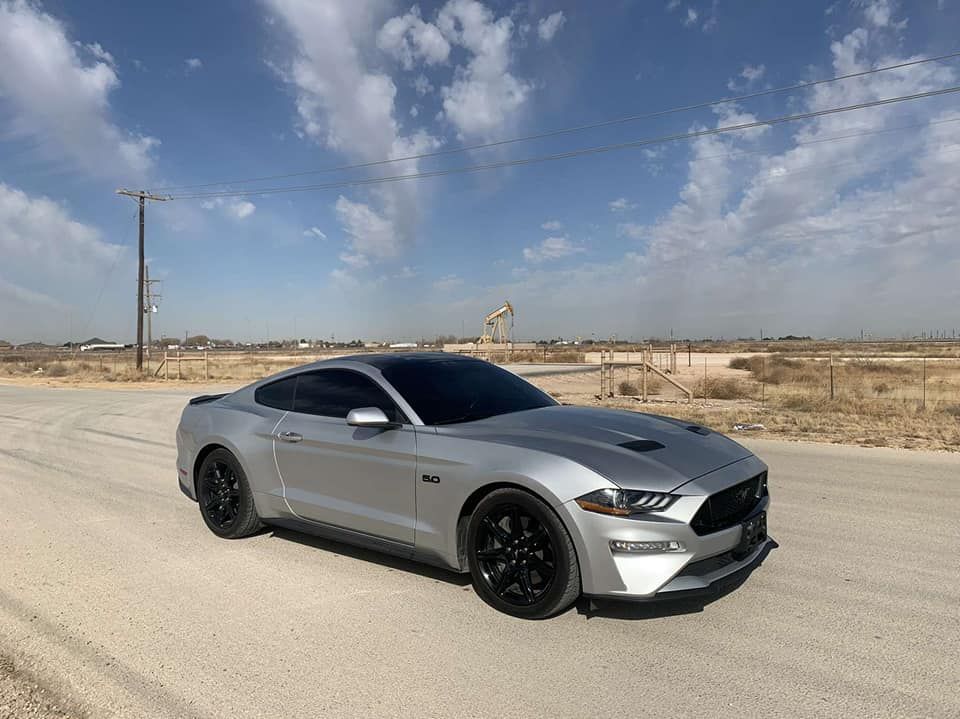 Silver sports car parked on a desert road under a partly cloudy sky