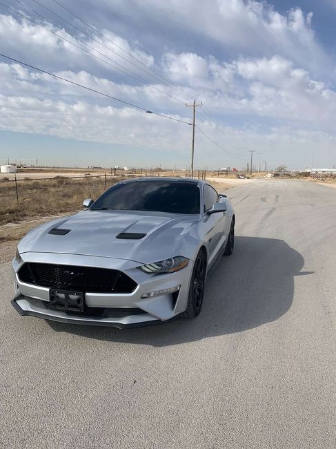 Silver sports car parked on a roadside under a cloudy sky in a пуст desert-like area