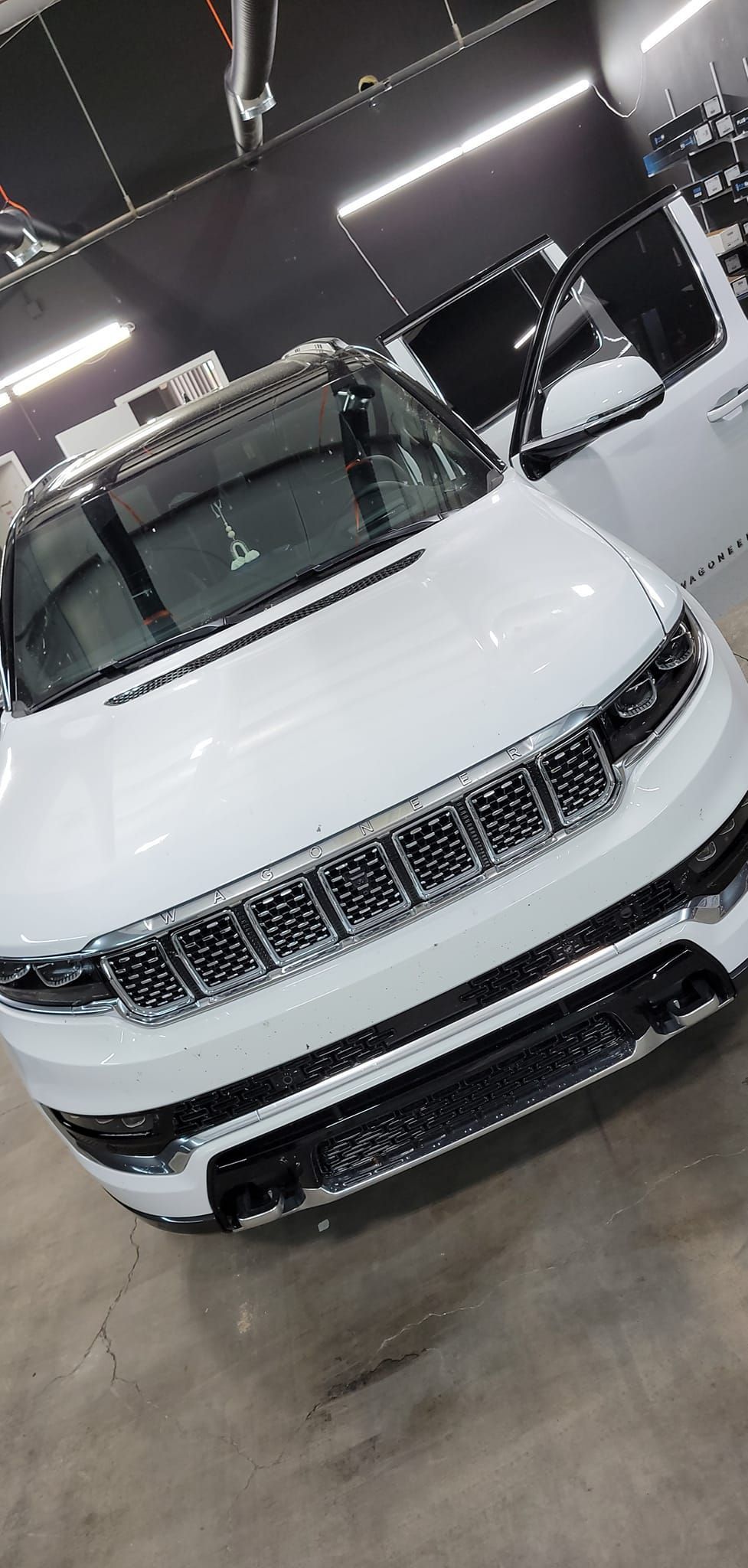 White SUV in a showroom, front view, under bright lights on a polished floor.
