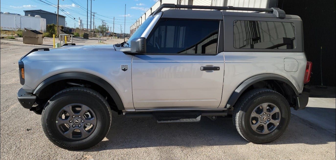 Side view of a silver and black SUV parked outdoors on a sunny street.