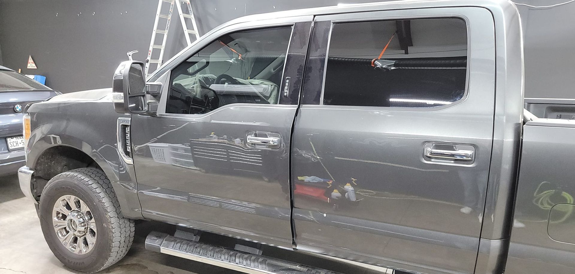Gray pickup truck with a damaged windshield and driver-side door at an indoor display