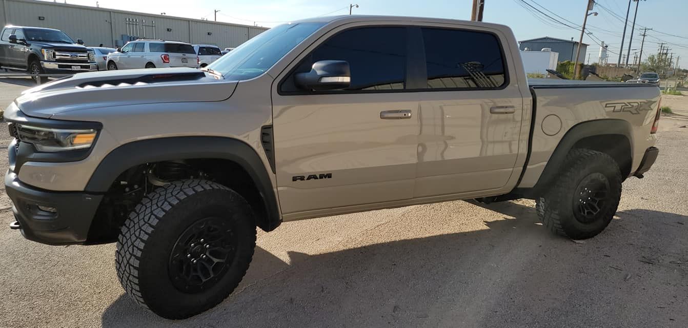 Tan lifted beige pickup truck parked on gravel with black wheels and tinted windows