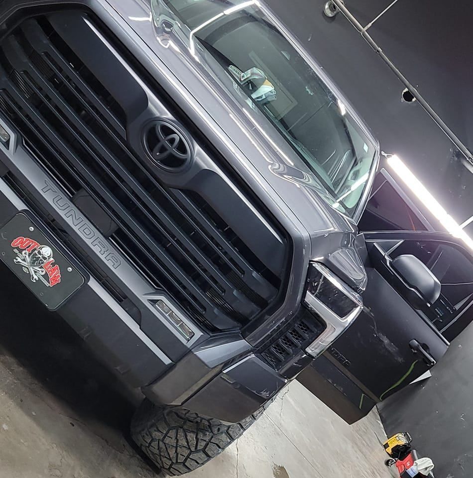 Black Toyota pickup truck in a garage, angled front view with off-road tires and open driver door
