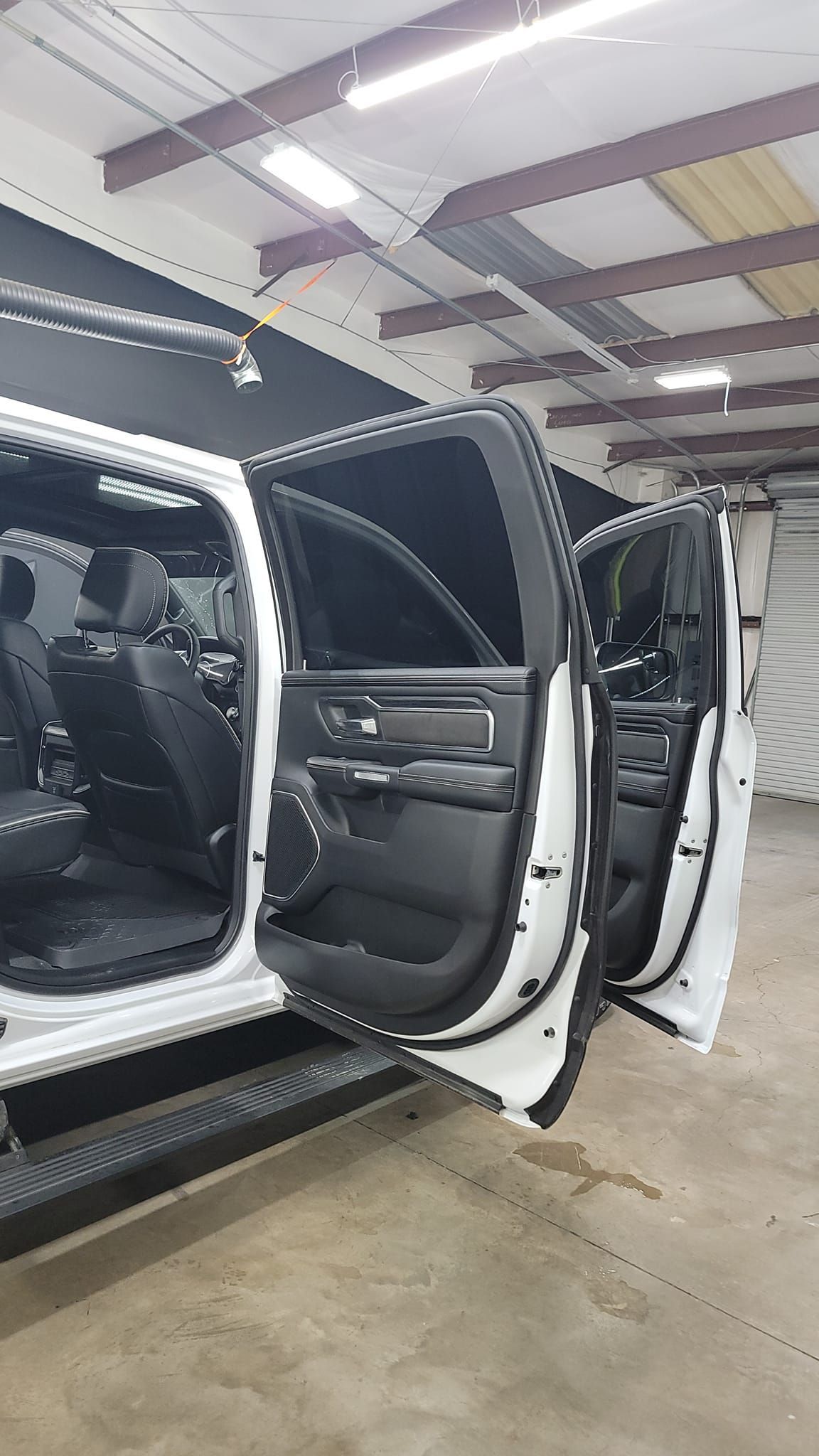 White SUV with all doors open inside a garage, showing a black interior under bright lights