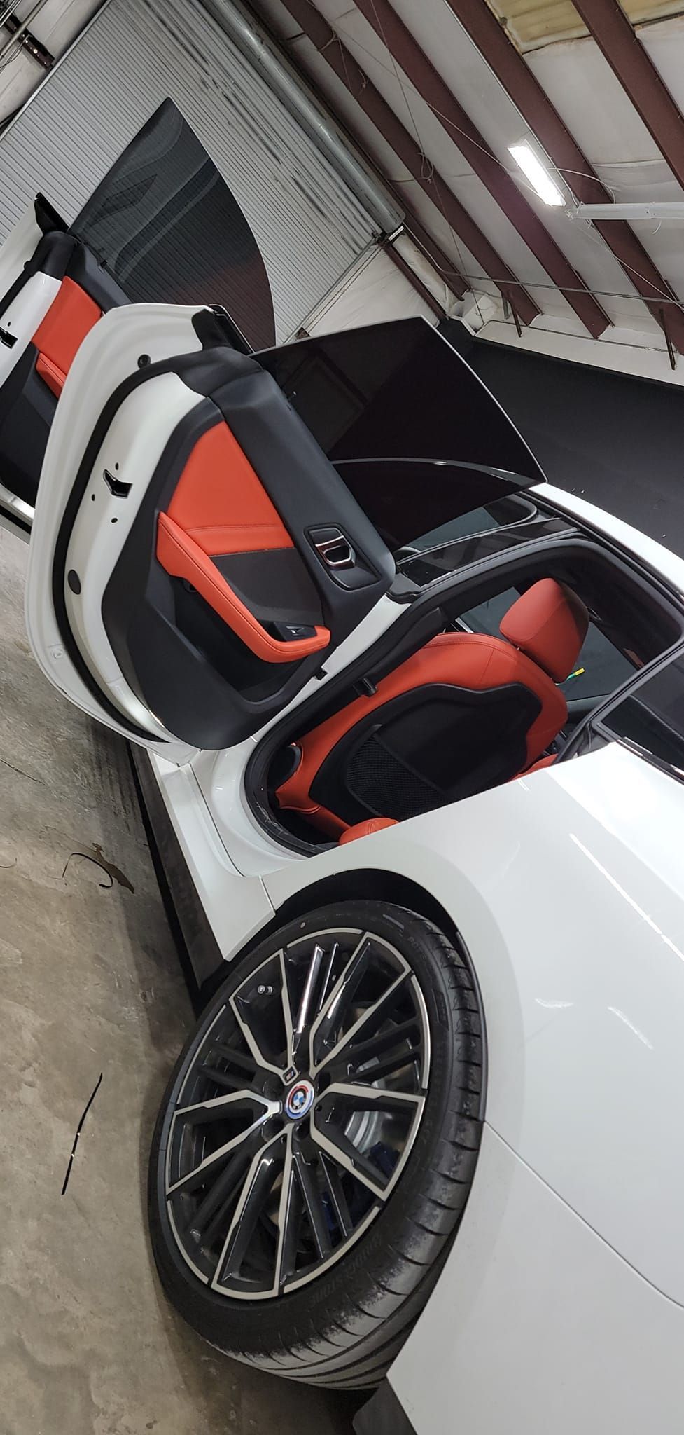 White sports car with scissor door open, showing red-and-black interior in a garage.