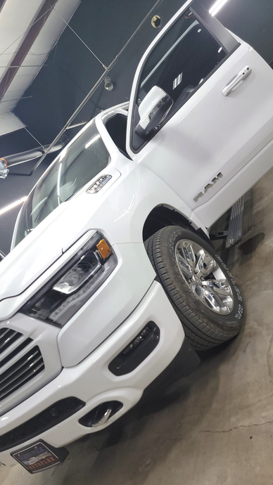 White pickup truck displayed indoors on a showroom floor, angled view with chrome wheels and grille.