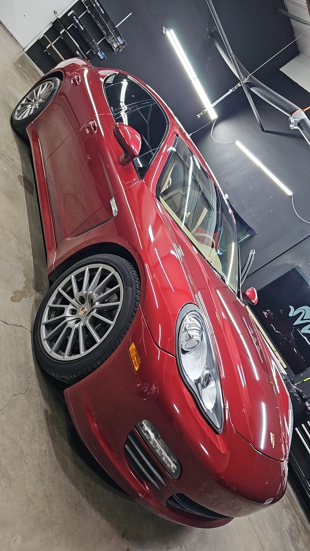Red sports car in a workshop, viewed from the front-left under bright lights.