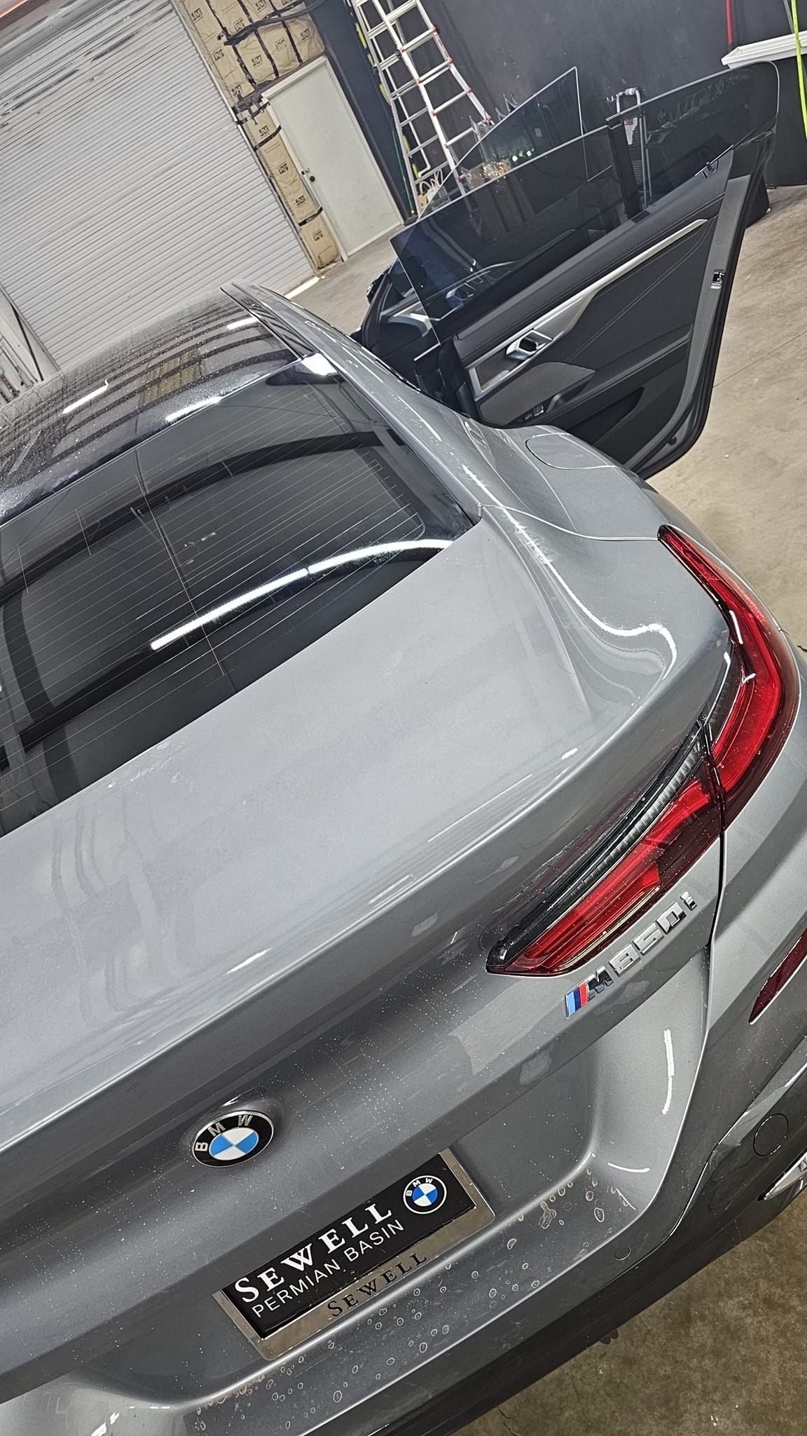 Gray BMW sedan with rear hatch open in a parking lot, viewed from above.