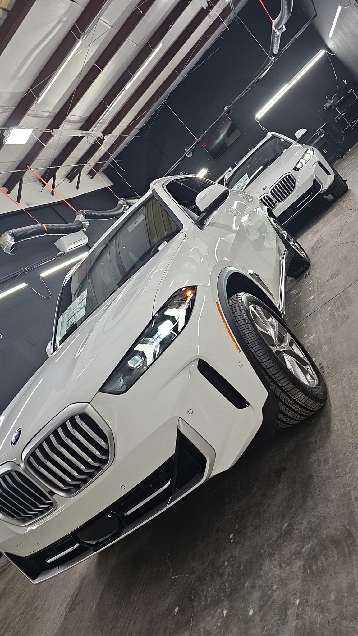 White luxury sedan displayed in a showroom, angled front view with bright overhead lights.