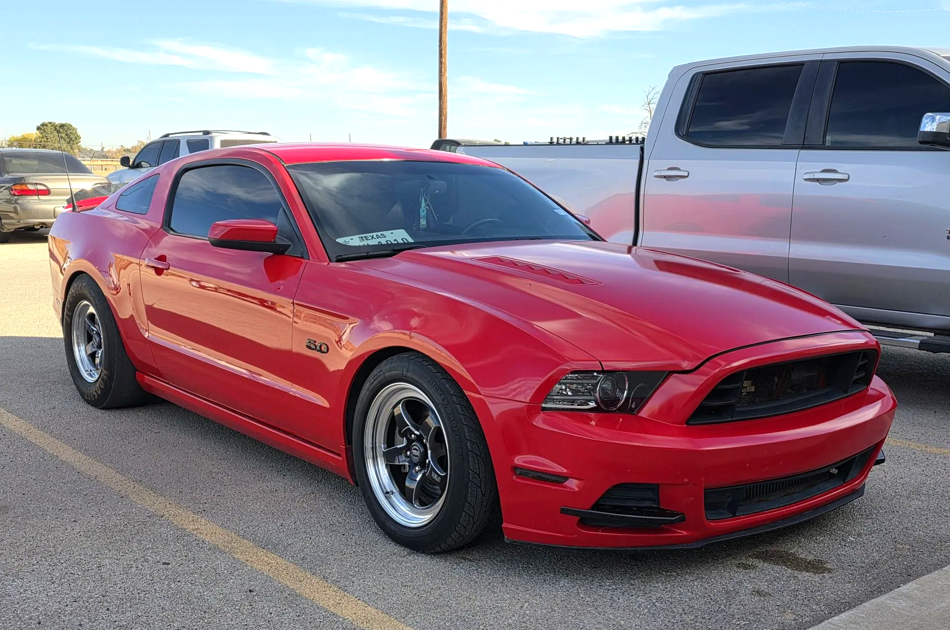 Red sports car parked in a lot beside a silver pickup truck at sunset