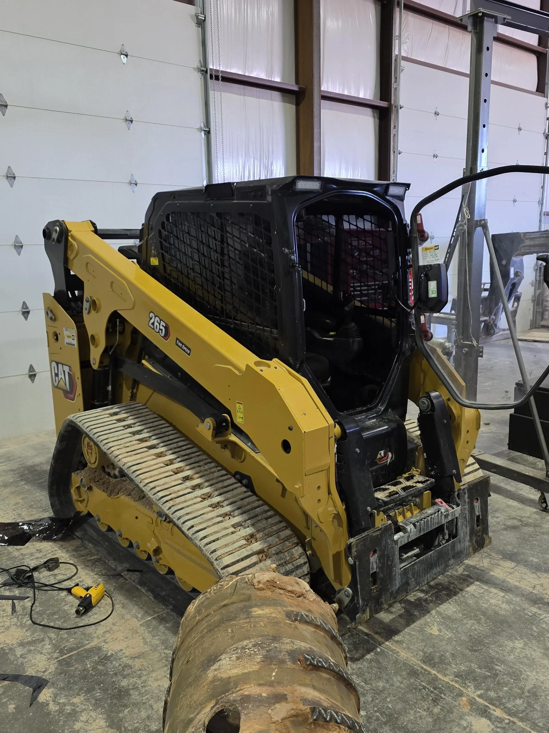 Yellow compact track loader inside a garage, with muddy tracks and bucket attached.