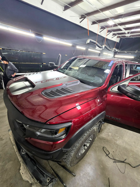 Red pickup truck in a garage, front hood open, with a black car beside it.