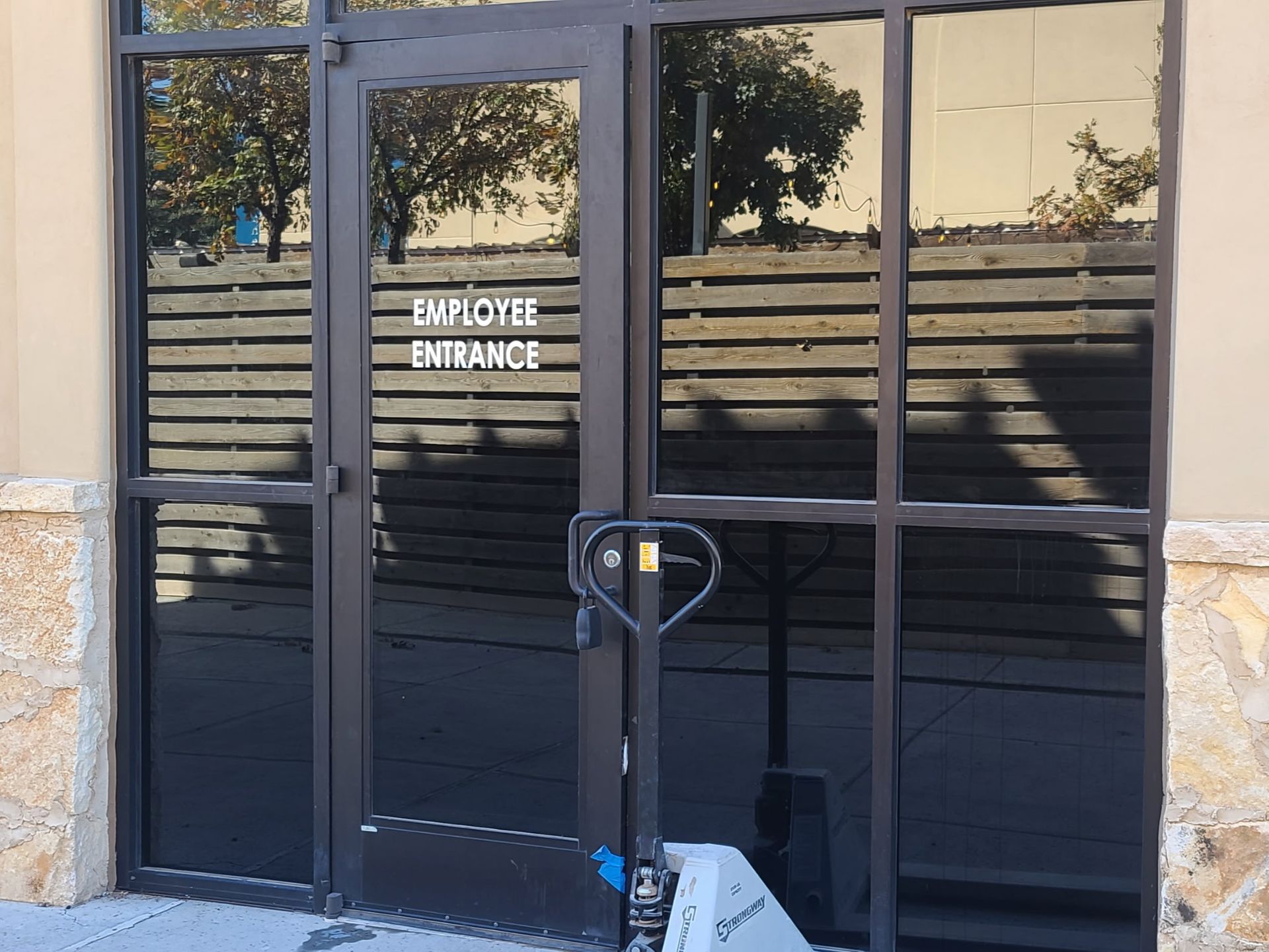 Glass storefront door labeled “Employee Entrance” with a black hand truck in front