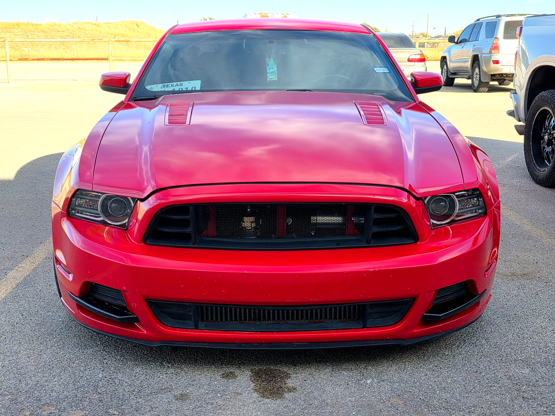 Red sports car parked in a lot, front view, with a black grille and hood scoop