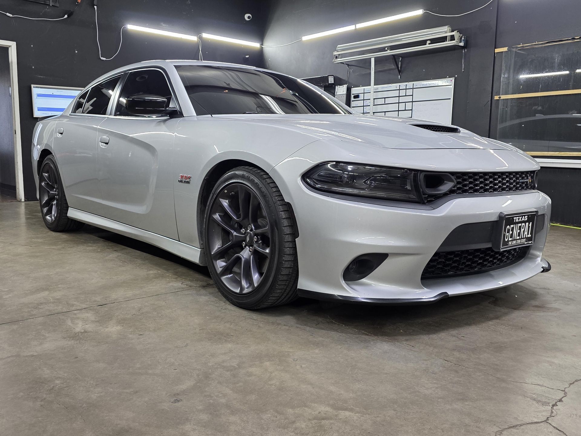 Silver Dodge Charger sedan in a garage, front three-quarter view with black wheels and bright headlights.