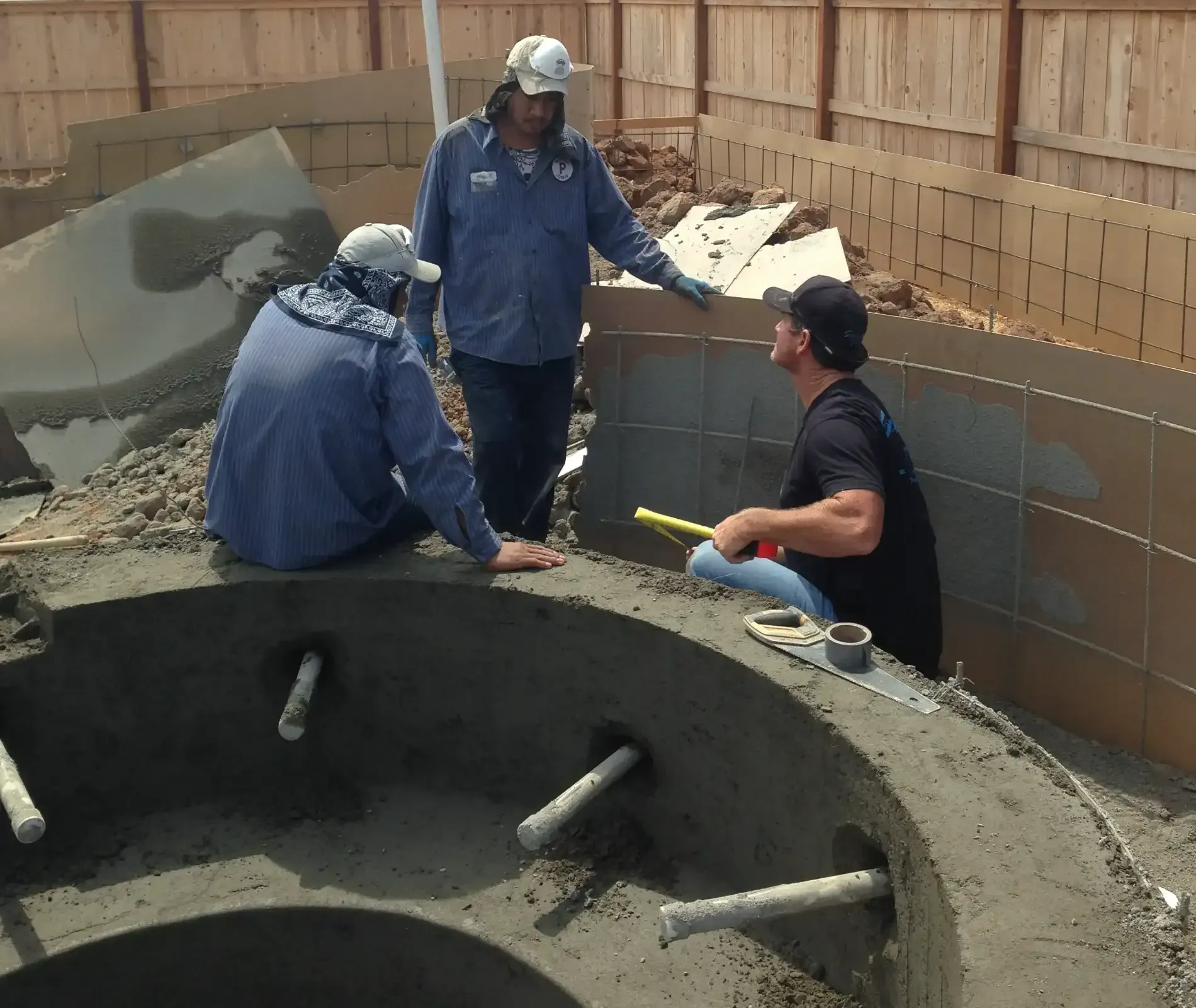 Workers inspecting a large concrete pit in a construction site, with tiles and wood framing around them.