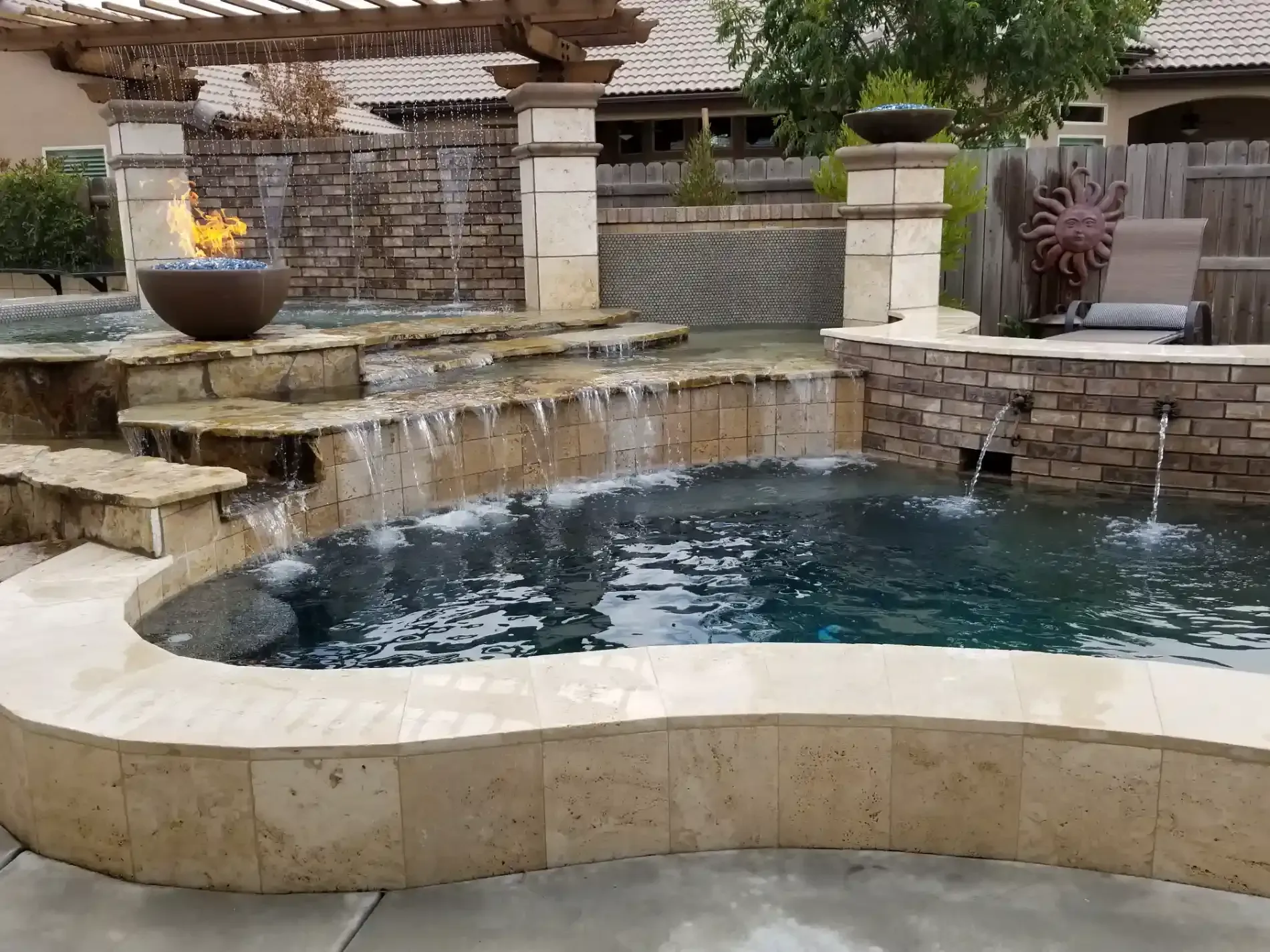 Backyard pool with stone waterfall, raised spa, and flame feature under a wooden pergola
