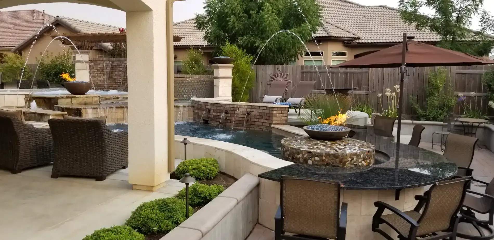 Backyard patio with wicker seating, stone fire pit, and outdoor dining table under umbrellas