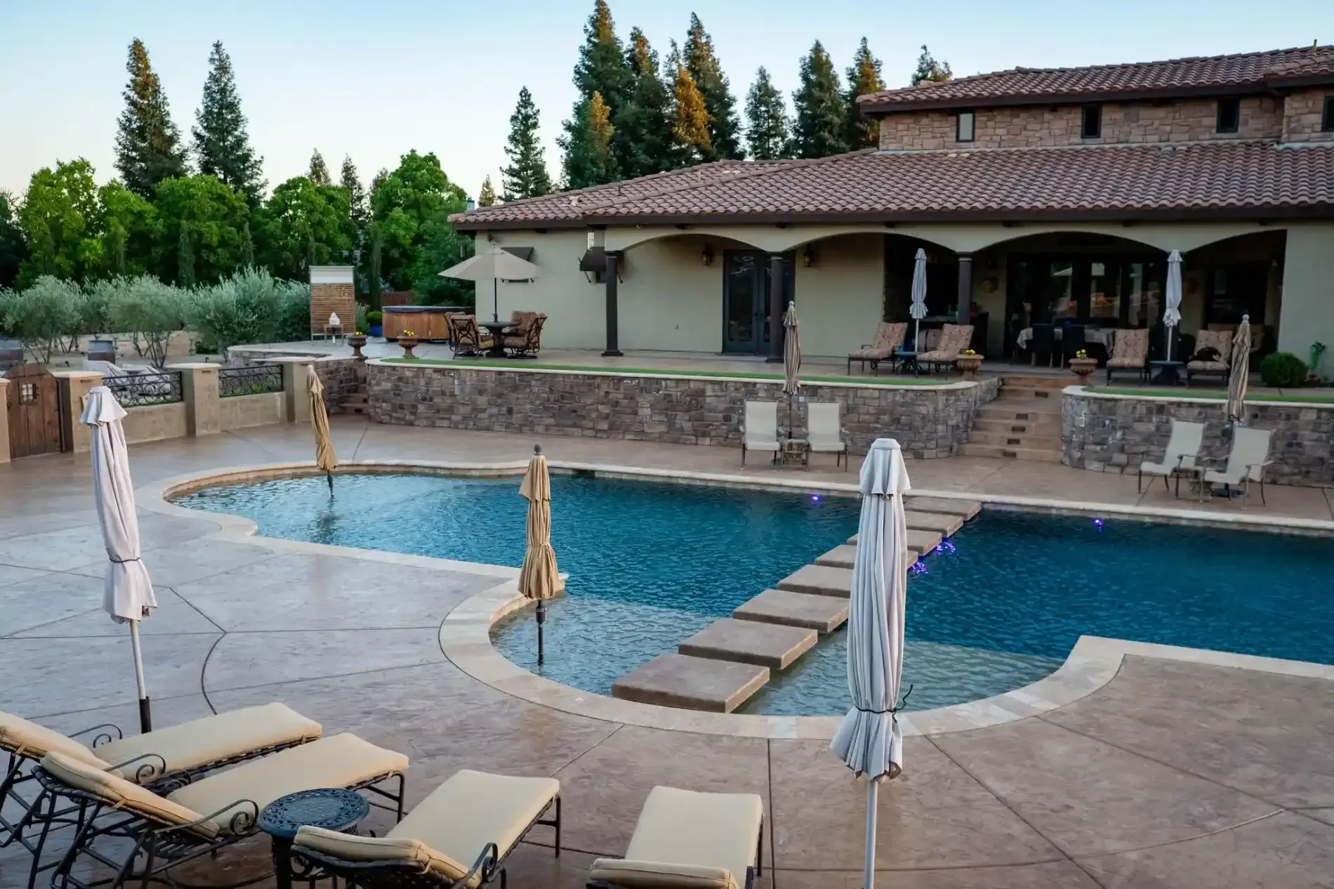 Backyard swimming pool with lounge chairs, umbrellas, and a stone patio beside a house