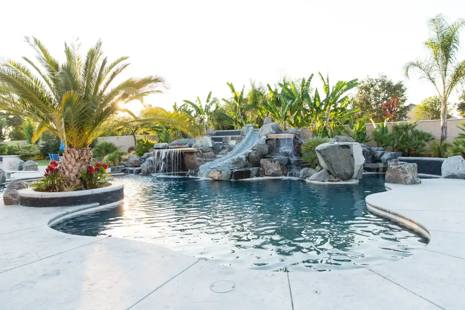 Backyard pool with waterfall rocks, palm trees, and white patio seating