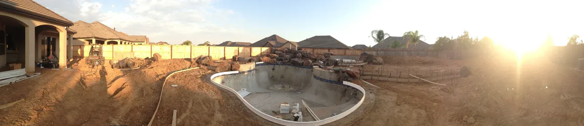 Sunlit backyard with a large round pool, patio, and distant mountains at sunset