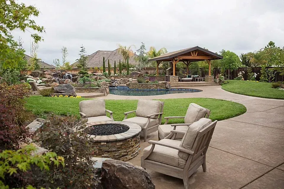 Patio with fire pit and cushioned chairs overlooking a landscaped backyard and gazebo